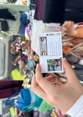 hand holding business card for Marias in front of table with artisanal mexican clothing