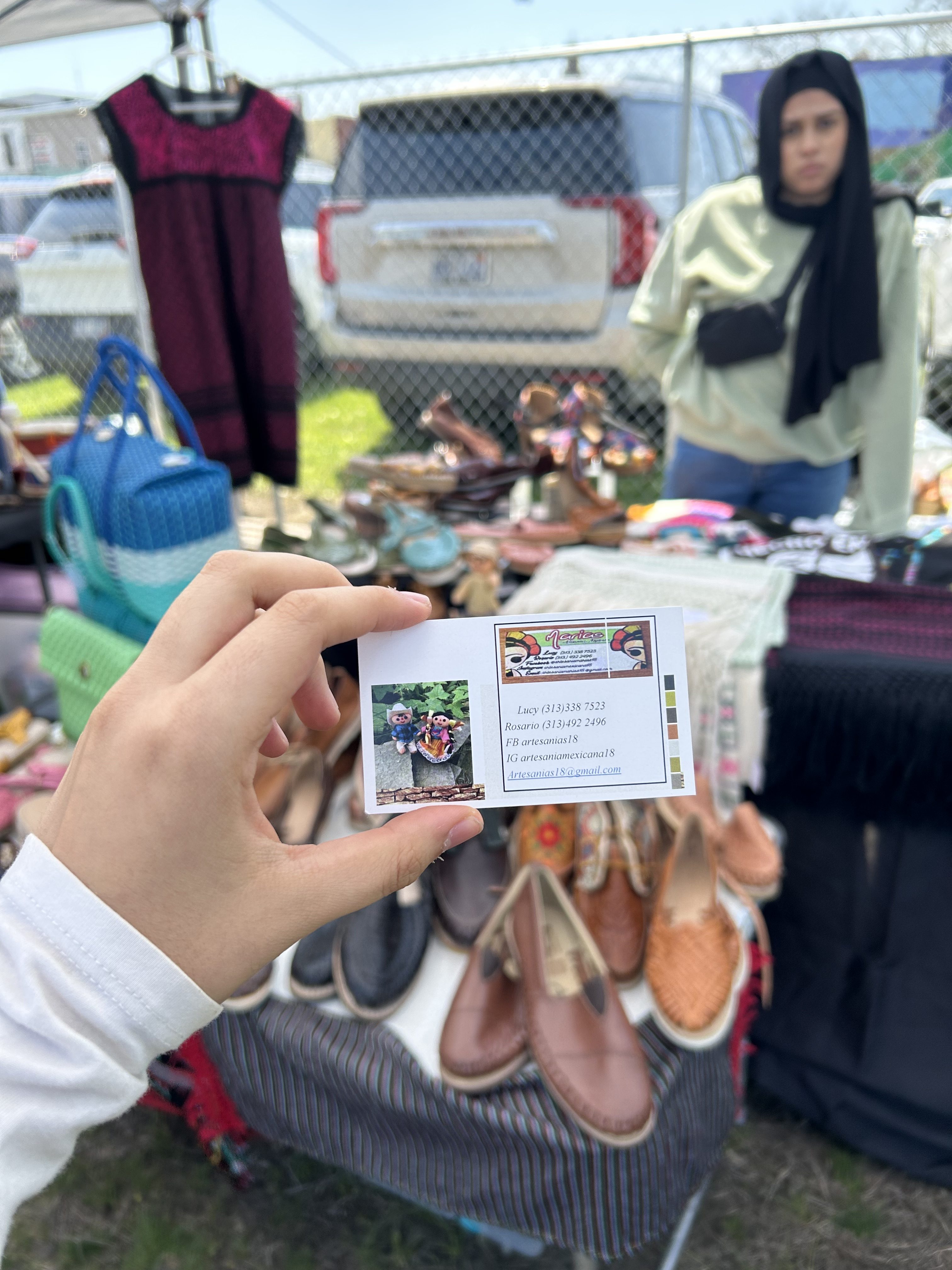 hand holding business card for Marias in front of table with artisanal mexican clothing