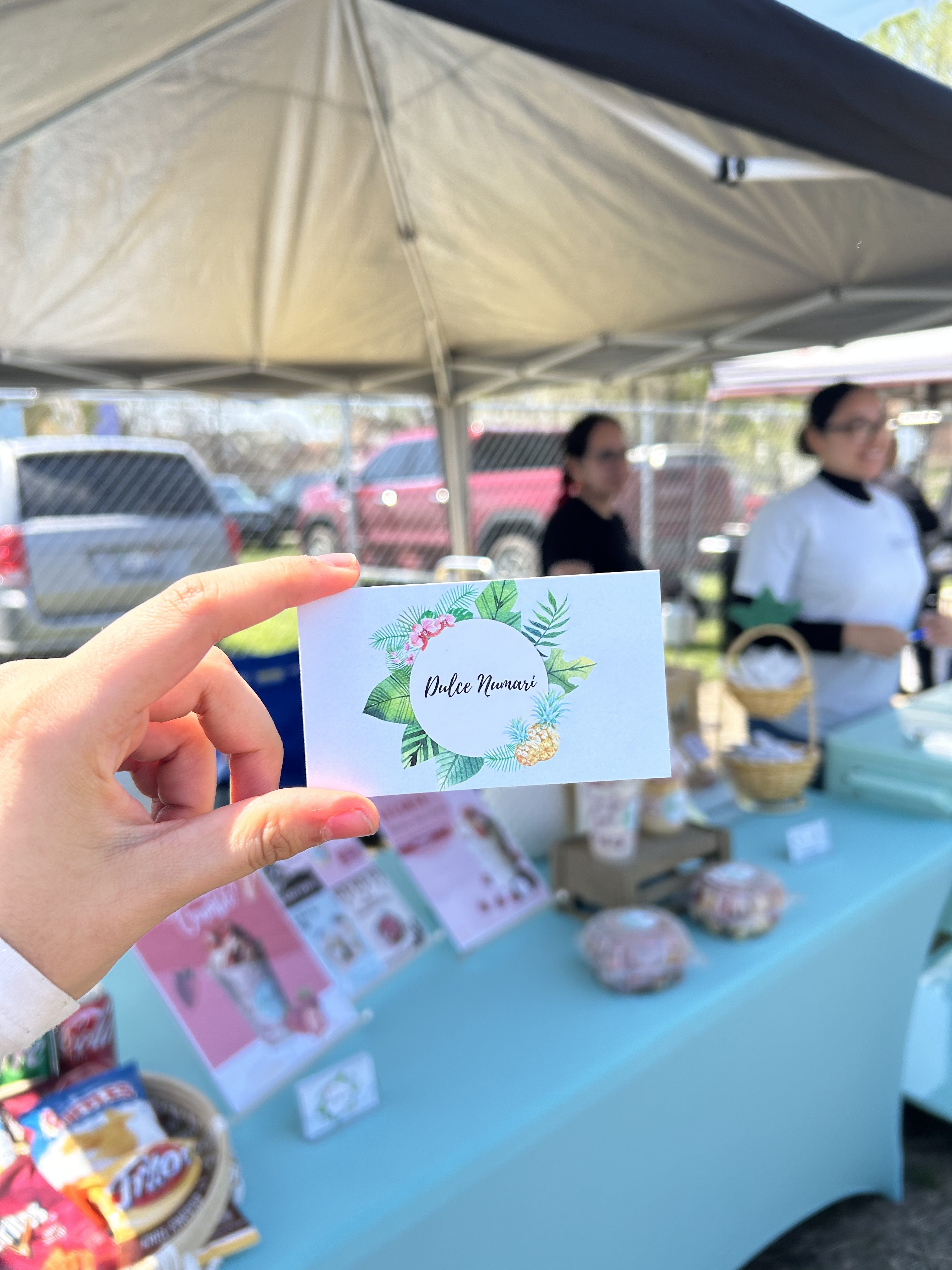 hand holding business card for Dulce Numari in front of table with homemade sweets